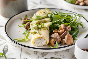 French rolled omelette stuffed with cream cheese with avocado, aragula and mushrooms for breakfast on white plate close up printed tile