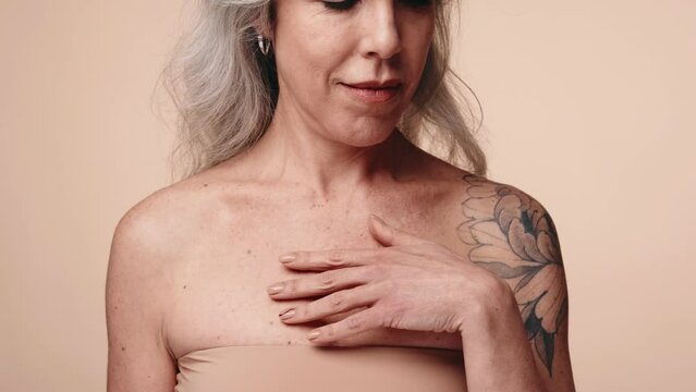 Closeup of graceful 50s woman with a floral tattoo, embodying mature beauty and confidence, touching skin on shoulders representing body positivity