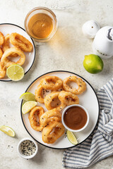 Crisp fried golden squid rings with lemon and sauce on a plate, light background top view