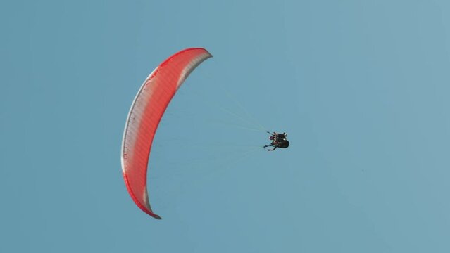 Red parachute flying against blue sky. Person paragliding in sky. Vertical video
