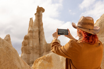 A woman in a brown jacket and hat is taking a picture of a mountain. The photo is in black and white