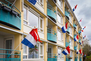 Dutch flags with an orange pennant on the facade of an apartment complex in the city of Deventer during King's Day - obrazy, fototapety, plakaty