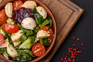 Delicious fresh caprese salad with mozzarella, tomatoes, greens with salt, spices and herbs