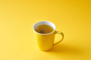 Tea bag in a yellow mug on a yellow background.