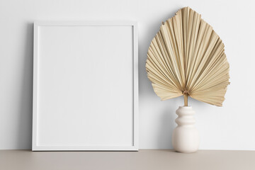 White frame mockup with a palm leaf decoration on the beige table.