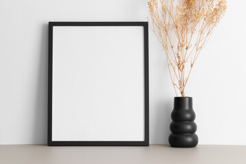Black frame mockup with a gypsophila decoration on the beige table.