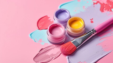 Obraz na płótnie Canvas Open jars of vibrant paints with a paintbrush on a pink background