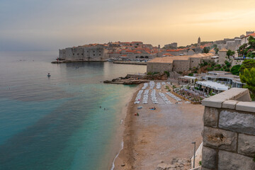 Sunset landscape with Banje beach and old town of Dubrovnik, Dalmatia, Croatia. Medieval fortress on the sea coast. Popular travel destination. Summer vacation background - 761769387