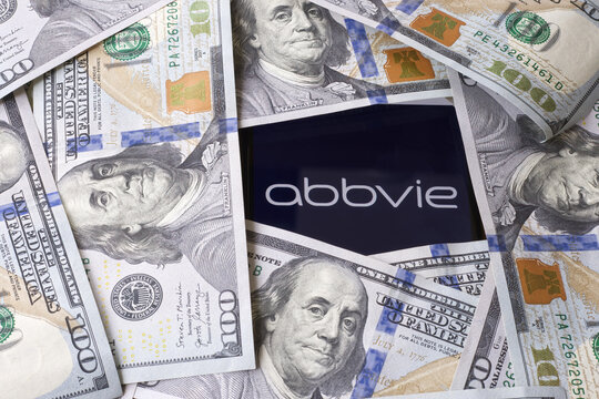 Abbvie logo is seen displayed on a smartphone lying under 100 dollar bills.