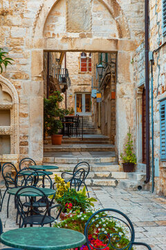 Fototapeta Sidewalk cafe with tables and chairs outside in old cozy street in the in old medieval town Hvar in outdoor restaurant with nobody, Dalmatia, Croatia. Vertical orientation. Popular travel destination