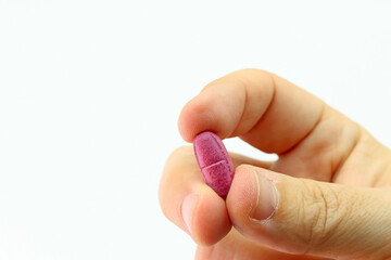 A hand holding a pink pill or medicine