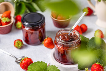 Fresh homemade strawberry jam in glass jar on a light background