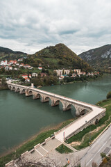 Fototapeta na wymiar Vertical shot of old Ottoman type bridge on a river with hills in background, river Drina in Visegrad