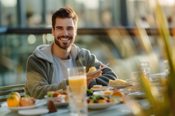 Fototapeta na wymiar Smiling young man with a beard having a delightful breakfast on a sunny terrace