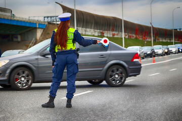 Obraz premium Policjantka ruchu drogowego z lizakiem podczas zatrzymania pojazdów na drodze z tarczą do zatrzymywania. 