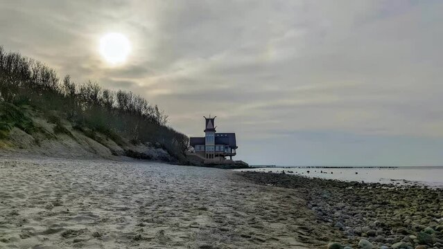 Tranquil parallax seascape of empty secluded sandy beach on Baltic Sea coast with old wooden house hotel on seafront at cloudy spring day. With no people panoramic shot rendered in 4K