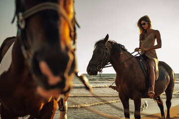 An attractive woman is horseback riding at the beach at sunset.