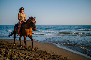 A seductive young lady is riding a horse on a beach near the sea.