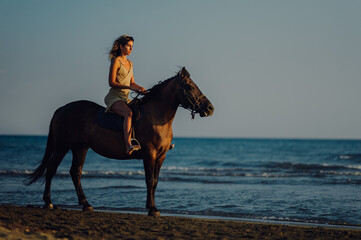 Side view of an equestrian riding a horse at the beach.