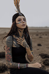 a woman with tattoos on her arms and face is sitting on a rock in the desert