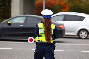 Policjantka ruchu drogowego z lizakiem podczas zatrzymania pojazdów na drodze z tarczą do zatrzymywania.
