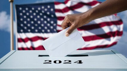 African American hand placing vote in ballot box with 2024 text for 2024 american presidential election with american flag in the background