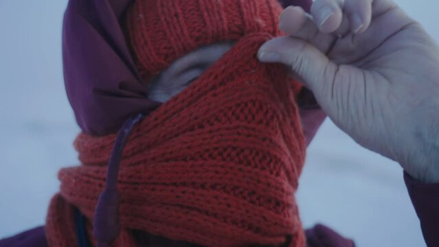 Elderly woman drawing red scarf on face. Puling scarf to protect skin from hard frost. Extreme cold in the North Pole. Traveling to the Arctic circle. People of the Northern areas. Dress warm. Winter