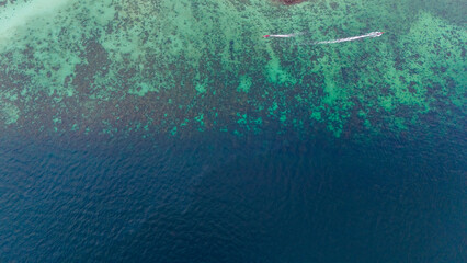 Boats crossing shallow waters of coral reef at the edge of deep blue sea. Aerial view, Phi Phi island, Krabi, Thailand.  