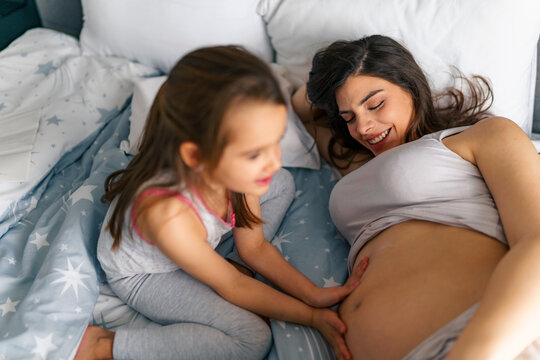 A picture of a pregnant mom smiling while her daughter rubs lotion on her belly or caressing the belly , spending quality time until the baby arrives