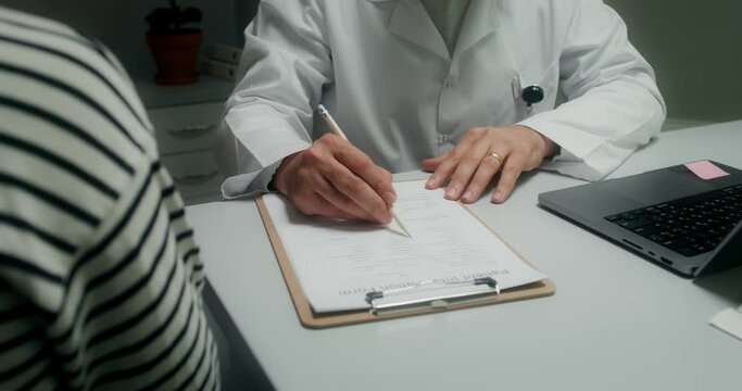A male doctor writes in a notebook, making an appointment for treatment to a patient. Close-up of his hands, an unrecognizable person