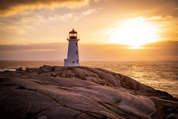 A beautiful sunset over the Atlantic Ocean at Peggy's Cove, Nova Scotia near Halifax with the iconic lighthouse in the foreground.