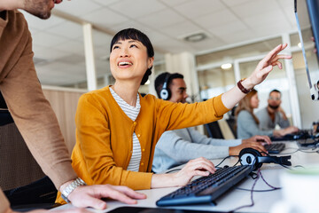 In their office, a multi-ethnic group of IT professionals works together, collaborating and using...