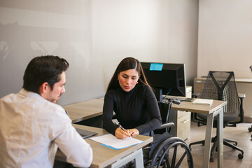 Beautiful Hispanic businesswoman in a wheelchair reviewing a contract with a client