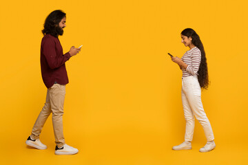 Two people standing back to back texting