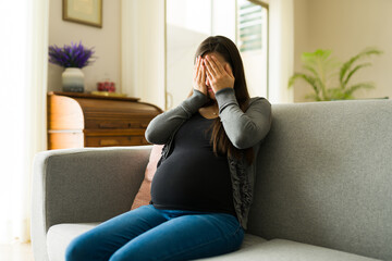 Sad pregnant woman with hormonal imbalance crying at home