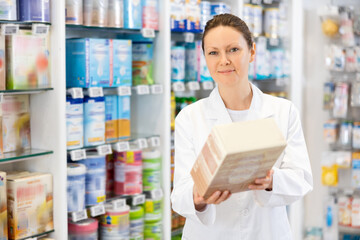 Adult female pharmacist in medical uniform posing with baby formula in her hands in pharmacy