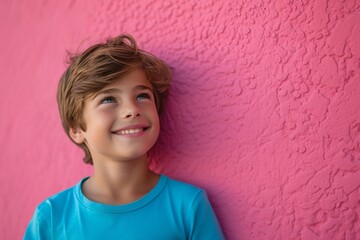 Happy little boy smiling while standing against a pink wall, portrait of joy and innocence