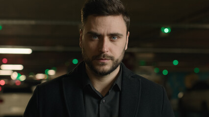 Fototapeta premium Portrait confident adult businessman business person millennial 30s man looking at camera serious face expression male driver professional employer entrepreneur in dark underground car parking outdoor
