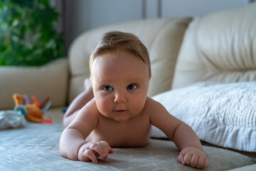 A curious baby with captivating eyes crawls on a bed, with toys scattered in the background suggesting playful activity