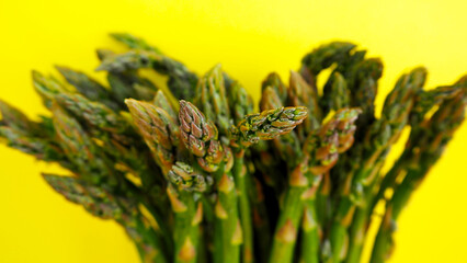 close by on a yellow background is a bunch of raw green asparagus pods. healthy food. side view. vegan . vegetables. copy space