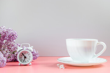 Alarm clock, lilac flowers and cup of coffee on light background.