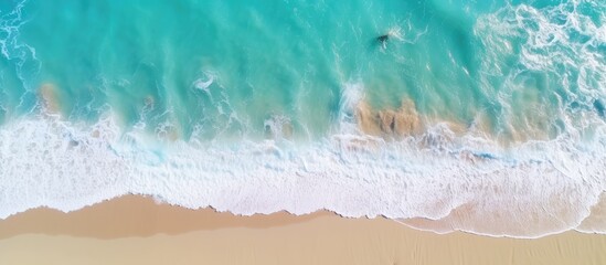 An aerial view of a sandy beach with azure waves crashing on the shore, creating a beautiful fluid pattern in the landscape