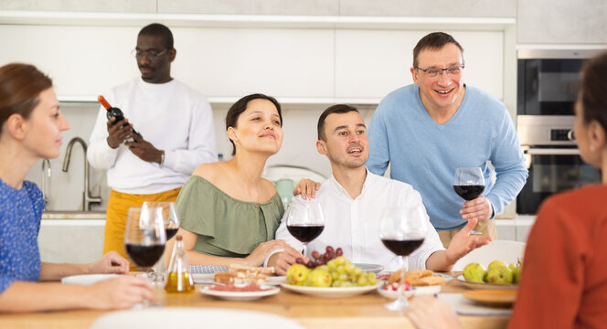 Ethnically diverse group of cheerful adult women and men engaging in casual banter and enjoying friendly company over wine 
