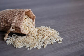 Closeup image of brown rice in small burlap sack on wooden table with copy space.