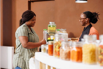 Smiling black woman shops at bio food market, buying fresh organic produce and supporting...