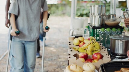 Multiracial volunteers provide hunger relief assistance to a caucasian woman on crutches and the...
