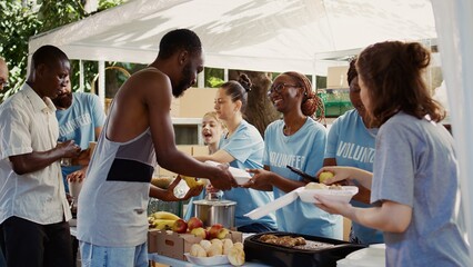 Multiethnic voluntary individuals distribute donated food, extending a helping hand to homeless and...