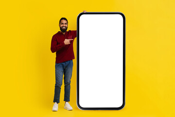 Cool eastern man pointing at huge smartphone with blank screen