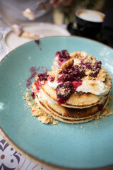 Close-up of pancakes with berry compote and cream on a blue plate