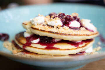 Close-up of pancakes with berry compote and cream on a blue plate